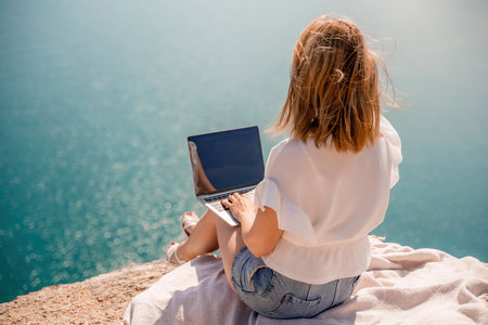 Freelance women sea working on the computer. Good looking middle aged woman typing on a laptop keyboard outdoors with a beautiful sea view. The concept of remote work.の写真素材