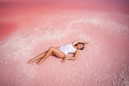 Woman in a pink salt lake. She lies in a white bathing suit. Wanderlust photo for memoryの写真素材