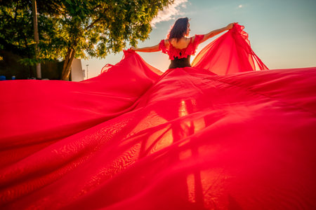 Sunrise red dress. A woman in a long red dress against the backdrop of sunrise, bright golden light of the suns rays. The concept of femininity, harmony.の写真素材