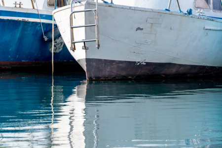 Reflection in the sea surface of white yachts parked in the port on the shore. Fragment of a ship on the water and the reflection of ships in the sea. motionless mirrored water of the seaの写真素材