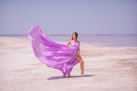 Woman in pink salt lake. She walks in a pink long dress and hat along the salty white shore of the lake. Wanderlust photo for memoryの写真素材