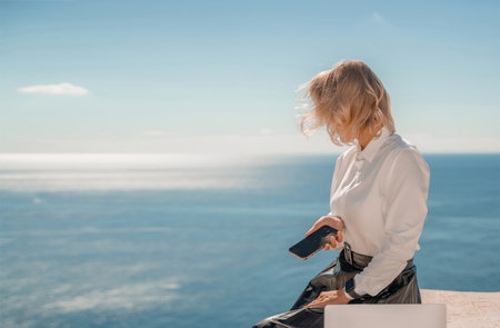 Freelance women sea working on a computer. Pretty middle aged woman with computer and phone outdoors with beautiful sea view. The concept of remote work.の写真素材