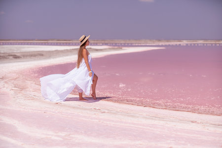 Woman in pink salt lake. She walks in a white long dress and hat along the salty white shore of the lake. Wanderlust photo for memoryの写真素材