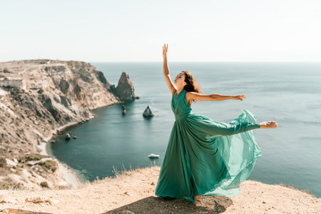 Woman green dress sea. Female dancer posing on a rocky outcrop high above the sea. Girl on the nature on blue sky background. Fashion photo.の写真素材