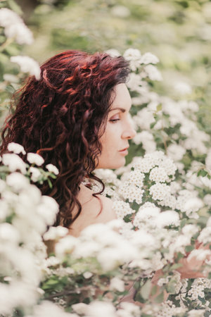Woman spirea flowers. Portrait of a curly happy woman in a flowering bush with white spirea flowers.の写真素材