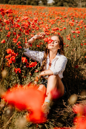 Woman poppies field. Happy woman is resting in the rays of the sun sitting in the poppy field.の写真素材