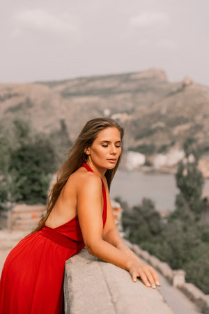 Woman red dress. Summer lifestyle of a happy woman posing near a fence with balusters over the sea.の写真素材