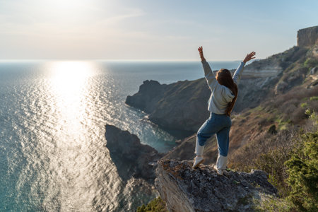 Woman tourist enjoying the sunset over the sea mountain landscape. Sits outdoors on a rock above the sea. She is wearing jeans and a blue hoodie. Healthy lifestyle, harmony and meditationの写真素材
