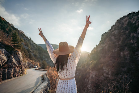 Woman road mountain. A woman in a white sweater, black boots and a hat walks along a winding alpine path between the mountains at sunset in late summer. The concept of travel.の写真素材