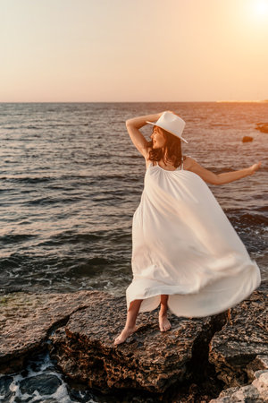 woman sea sunset. A woman in a dress, hat and with a straw bag is standing on the beach enjoying the sea. Happy summer holidays.の写真素材
