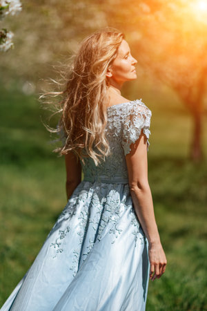 Blond garden. Portrait of a blonde in the park. Happy woman with long blond hair in a blue dress.の写真素材