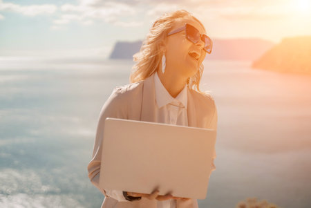 Freelance women sea. She is working on the computer. Good looking middle aged woman typing on a laptop keyboard outdoors with a beautiful sea view. The concept of remote work.の写真素材