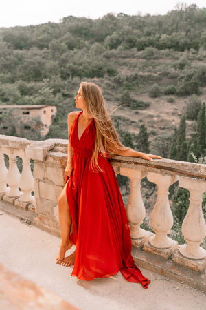 Woman red dress. Summer lifestyle of a happy woman posing near a fence with balusters over the sea.の写真素材