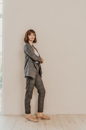Brunette suit wall. Business woman in a beige suit posing on a beige background. Full length studio portrait.の写真素材