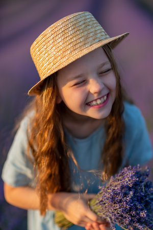 Lavender sunset girl. A laughing girl in a blue dress with flowing hair in a hat walks through a lilac field, holds a bouquet of lavender in her hands.の写真素材