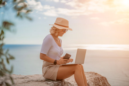 Freelance women sea working on the computer. Good looking middle aged woman typing on a laptop keyboard outdoors with a beautiful sea view. The concept of remote work.の写真素材
