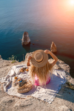 woman sea travel. photo of a beautiful woman with long blond hair in a pink shirt and denim shorts and a hat having a picnic on a hill overlooking the seaの写真素材