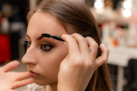 Make-up artist paints eyebrow pencil to beautiful brunette in beの写真素材
