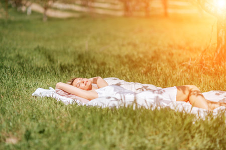 woman garden. she sleeps on a white bed in the fresh spring grass in the garden. Dressed in a blue nightgown.の写真素材