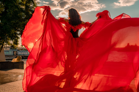 Sunrise red dress. A woman in a long red dress against the backdrop of sunrise, bright golden light of the suns rays. The concept of femininity, harmony.の写真素材
