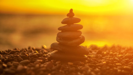 Balanced rock pyramid on pebbles beach. Golden sea bokeh on background. Selective focus, zen stones on sea beach, meditation, spa, harmony, calm, balance concept.の写真素材