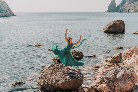 Female dancer in a long mint dress posing on a beach with rocks on sunny day. Girl on the nature on blue sky background.の写真素材
