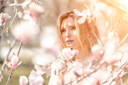Magnolia woman portrait. Happy middle aged woman enjoying the smell in a blooming spring garden. Beautiful magnolia bushes, large flowers.の写真素材