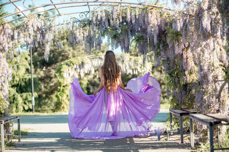 Woman wisteria lilac dress. Thoughtful happy mature woman in purple dress surrounded by chinese wisteriaの写真素材