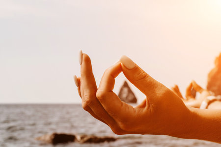 Yoga on the beach. A happy woman meditating in a yoga pose on the beach, surrounded by the ocean and rock mountains, promoting a healthy lifestyle outdoors in nature, and inspiring fitness concept.の写真素材
