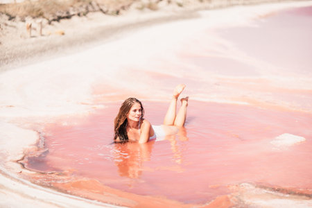 Woman in a pink salt lake. She lies in a white bathing suit. Wanderlust photo for memory