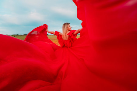 Woman Red Flying Dress. A blonde in a red dress against the sky. Rear view of a beautiful blonde woman in a red dress fluttering in the wind against a blue sky and clouds.の写真素材