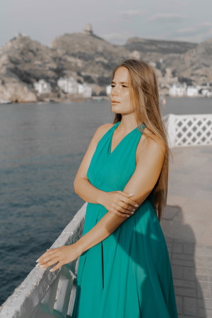 Woman sea green dress. Side view a happy woman with long hair in a long mint dress posing on a beach with calm sea bokeh lights on sunny day. Girl on the nature on blue sky background.の写真素材