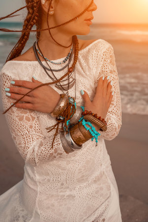 Model in boho style in a white long dress and silver jewelry on the beach. Her hair is braided, and there are many bracelets on her arms.の写真素材