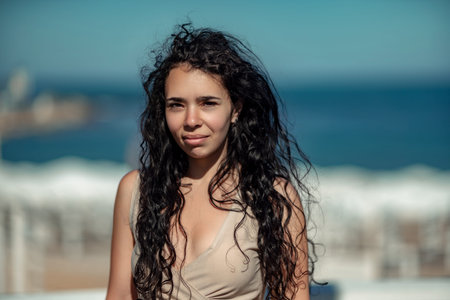 Sea woman rest. Portrait of a woman with long curly black hair in a beige dress stands on a balcony...