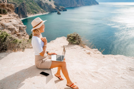 Freelance women sea working on the computer. Good looking middle aged woman typing on a laptop keyboard outdoors with a beautiful sea view. The concept of remote work.の写真素材