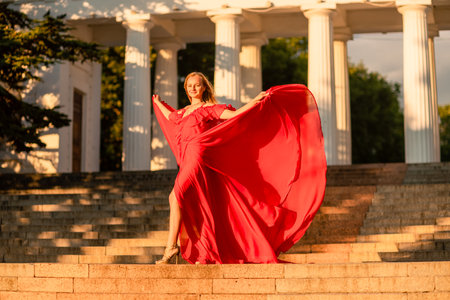 A woman in a long red dress against the backdrop of sunrise, bright golden light of the suns rays. The concept of femininity, harmony.の写真素材