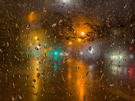 Rain bokeh road lights. Abstract shot of evening city traffic bokeh. Multicolored lights of the evening city and passing cars through a wet rainy window.の写真素材