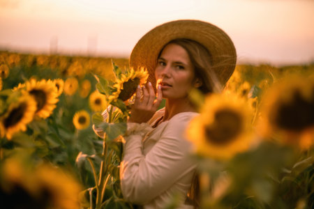 Beautiful middle aged woman looks good in a hat enjoying nature in a field of sunflowers at sunset. Summer. Attractive brunette with long healthy hair.の写真素材