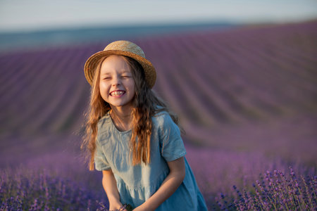 Lavender sunset girl. A laughing girl in a blue dress with flowing hair in a hat walks through a lilac field, holds a bouquet of lavender in her hands.の写真素材