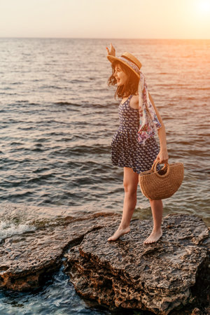 A woman in a dress, hat and with a straw bag is standing on theの写真素材