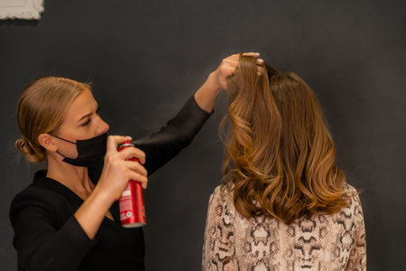 Women salon hairstyle. Hairdresser uses hairspray on clients hair in salon, Portrait of two beautiful womenの写真素材