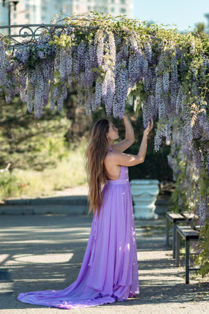 Woman wisteria lilac dress. Thoughtful happy mature woman in purple dress surrounded by chinese wisteriaの写真素材