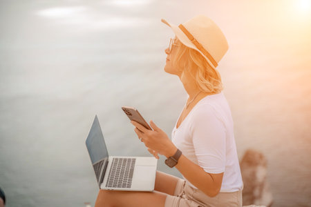Freelance women sea working on the computer. Good looking middle aged woman typing on a laptop keyboard outdoors with a beautiful sea view. The concept of remote work.の写真素材