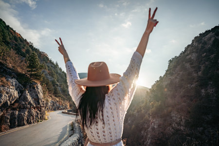 Woman road mountain. A woman in a white sweater, black boots and a hat walks along a winding alpine path between the mountains at sunset in late summer. The concept of travel.の写真素材