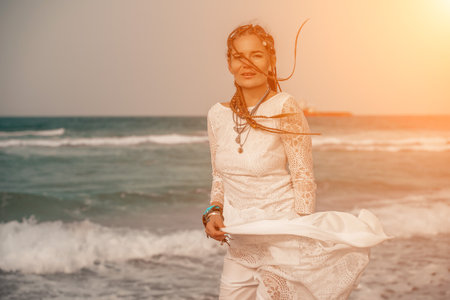 Model in boho style in a white long dress and silver jewelry on the beach. Her hair is braided, and there are many bracelets on her arms.の写真素材