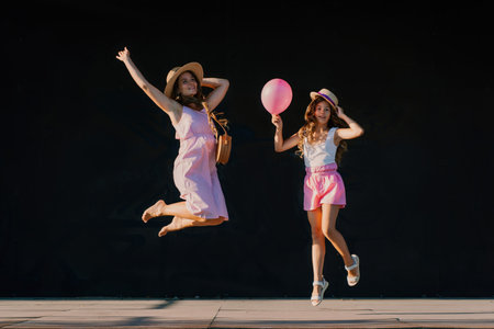 mother and daughter jumping in pink dresses with loose long hair on a black background. Enjoy communicating with each otherの写真素材