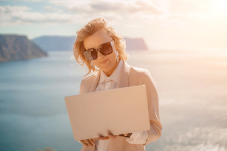 Freelance women sea. She is working on the computer. Good looking middle aged woman typing on a laptop keyboard outdoors with a beautiful sea view. The concept of remote work.の写真素材