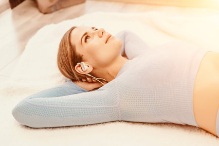 Top view portrait of relaxed woman listening to music with headphones lying on carpet at home. She...