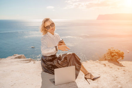 Freelance women sea working on a computer. Pretty middle aged woman with computer and phone outdoors...