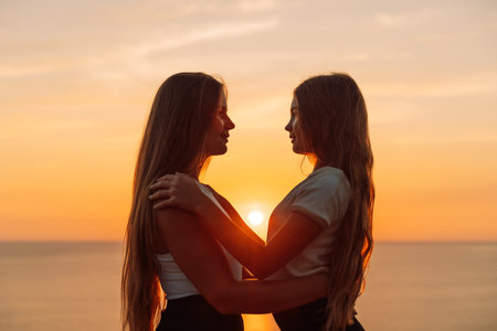 Mother daughter sunset. Mother and daughter stand on the beach, hugging and looking at each other enjoying the sunset.の写真素材